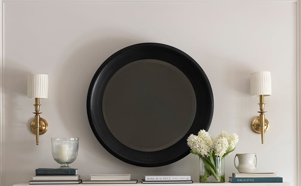 Classic symmetrical mantel decor with matching brass sconces and a centered round mirror