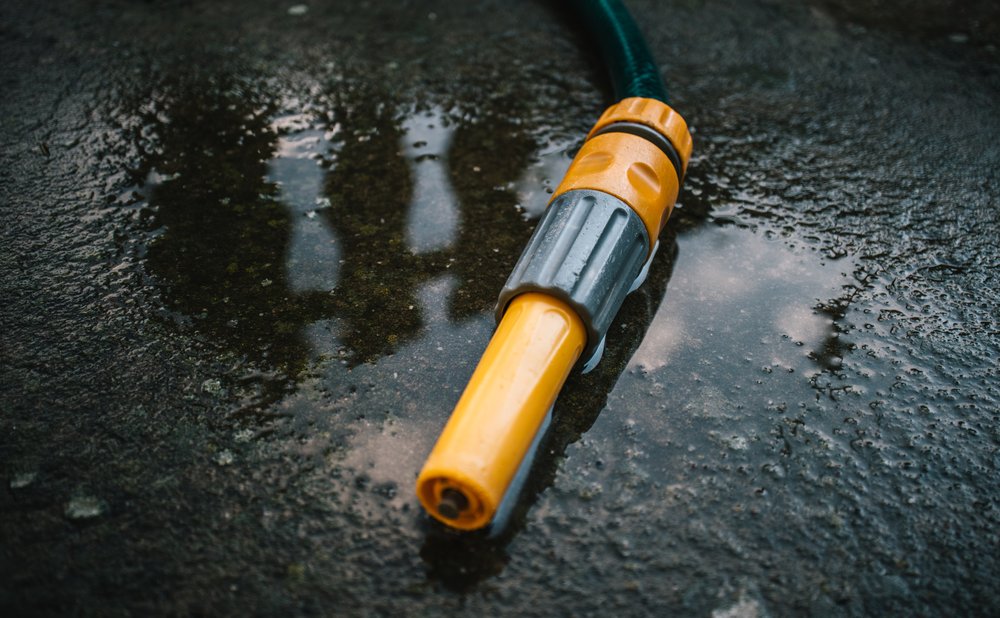 Gloves, gutter scoop, bucket and garden hose laid out as tools to clean gutters