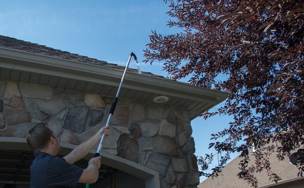 Homeowner using a telescoping wand to clean gutters from the ground
