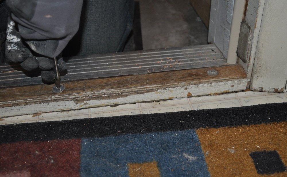 Screwdriver adjusting a door threshold to close the gap under an entry door