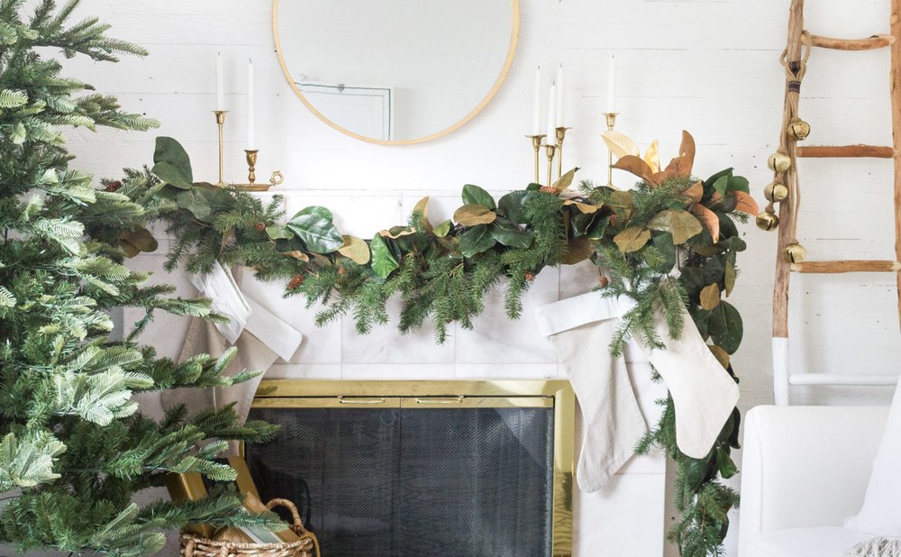 Fireplace mantel draped with a full magnolia leaf and pine garland under a round brass mirror