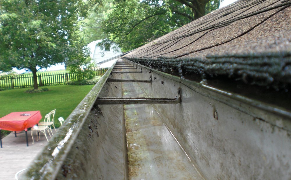 Garden hose flushing a clean gutter to check the water flow toward the downspout