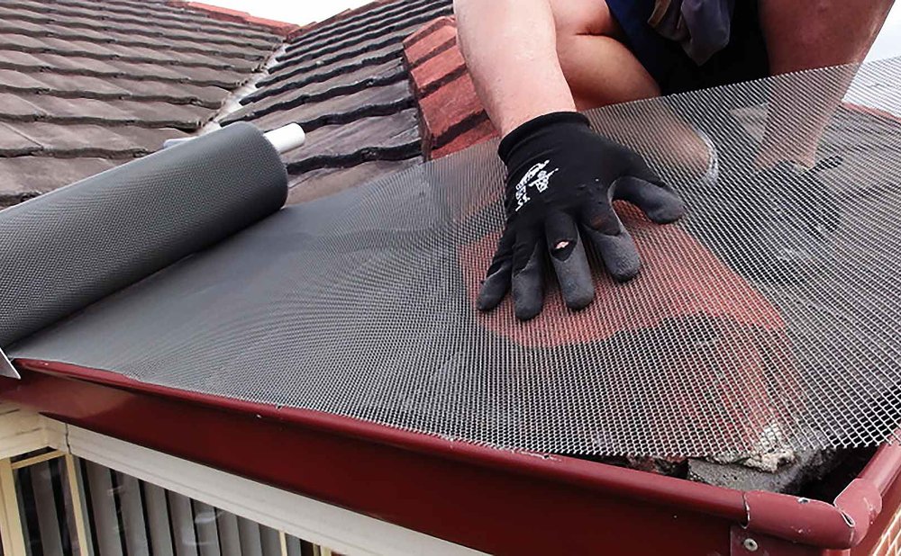 Brush sweeping leaves off mesh gutter guards on a roof edge