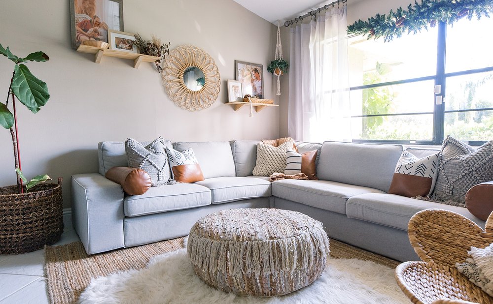 Boho living room with a grey sectional, woven pouf, rattan chair and sunburst mirror