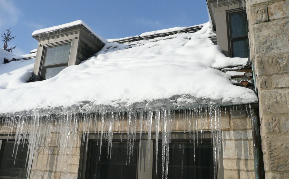 Ice dam and icicles along a roof edge above a gutter in winter