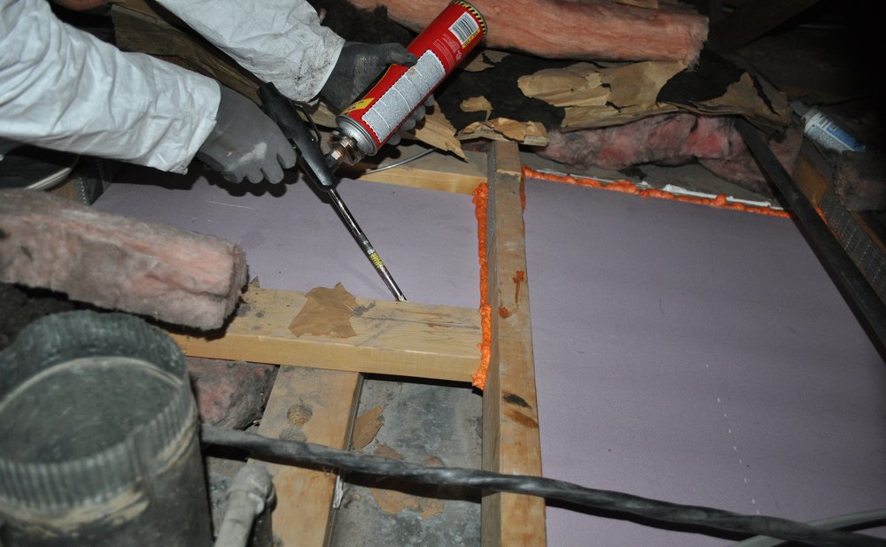 Spray foam sealing a gap around a pipe where it enters the house