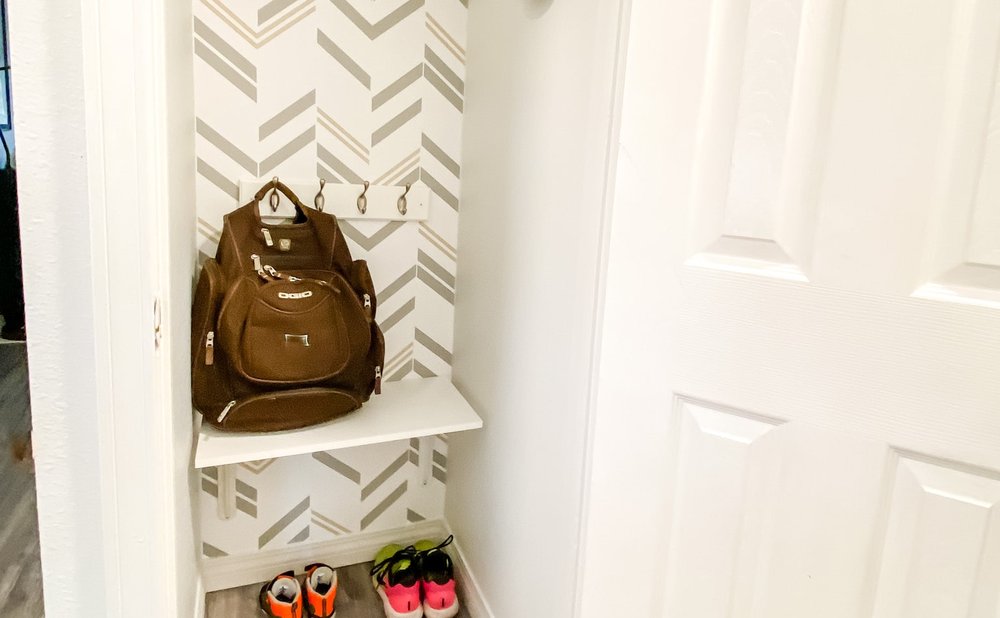 Front hall closet converted to a mudroom nook with a bench, hooks and wallpaper