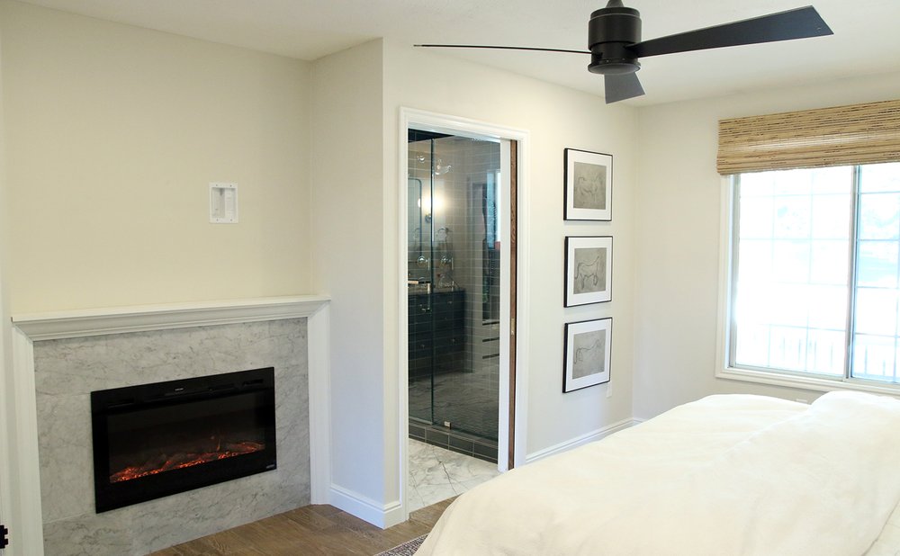 Electric fireplace with a white marble surround and painted wood mantel in a bedroom corner